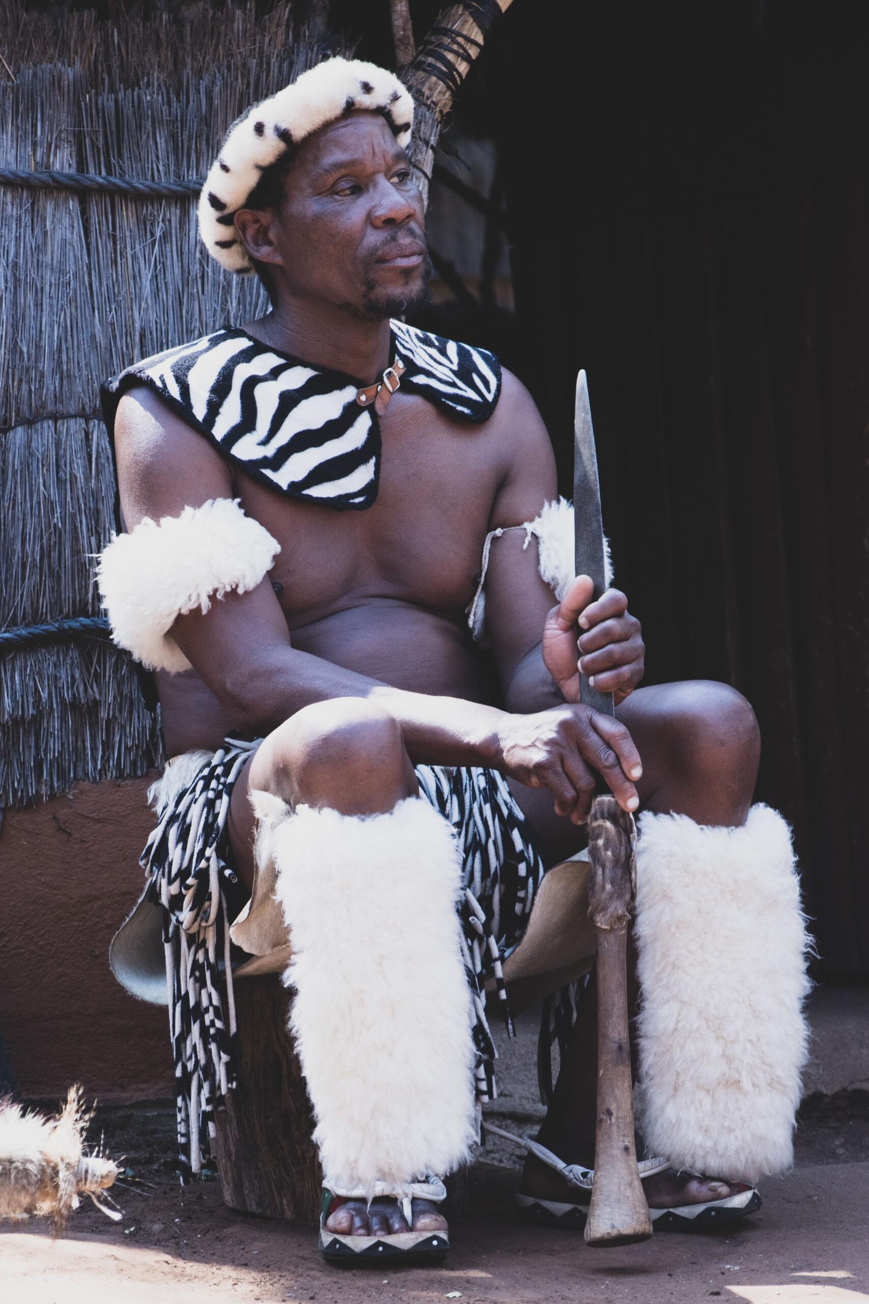 An image of an African chief outside of a grass hut and dressed in traditional regalia.