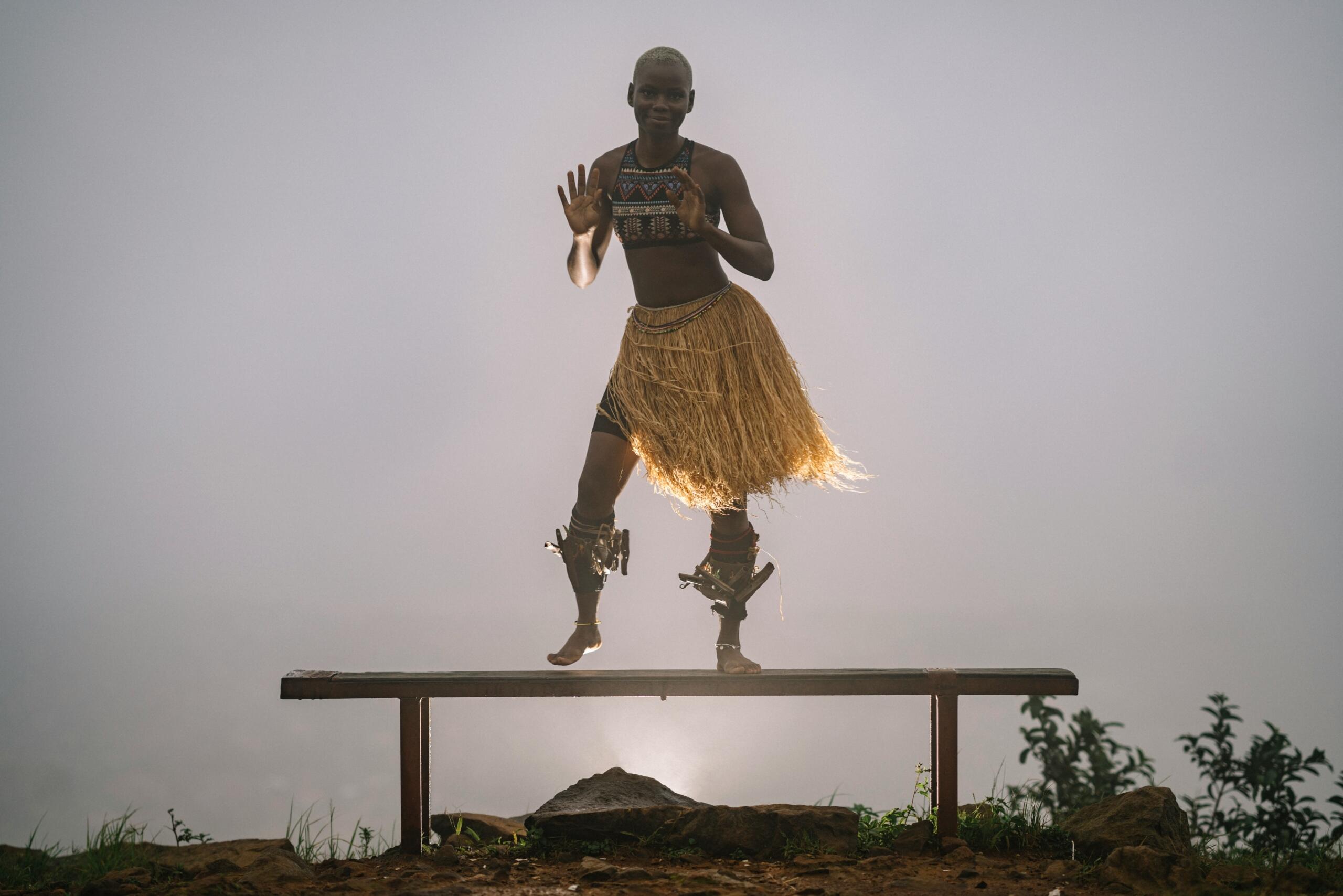 African performer dancing on a raised platform in traditional clothing.