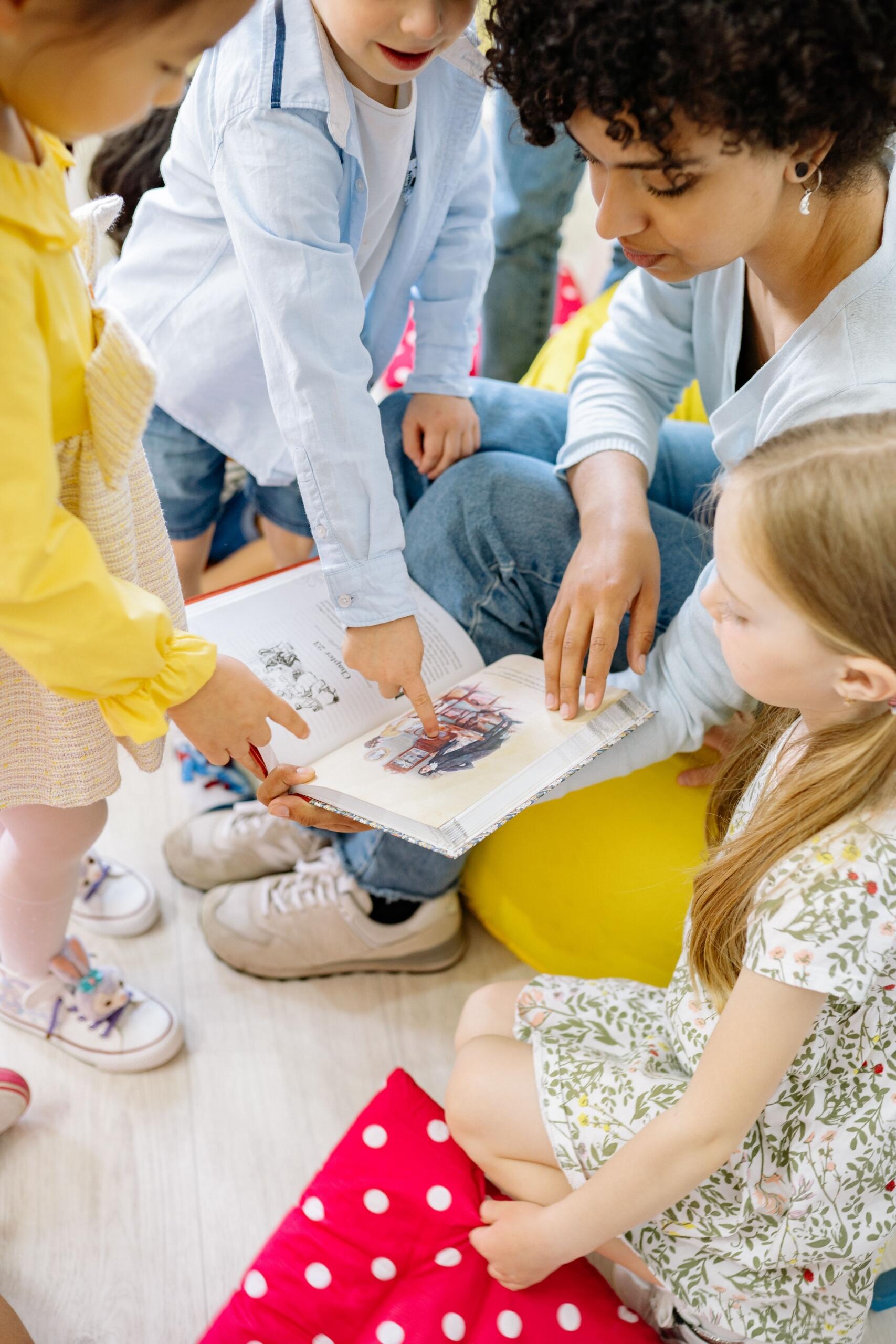 group of young children gathered around a woman paging through a picture storybook