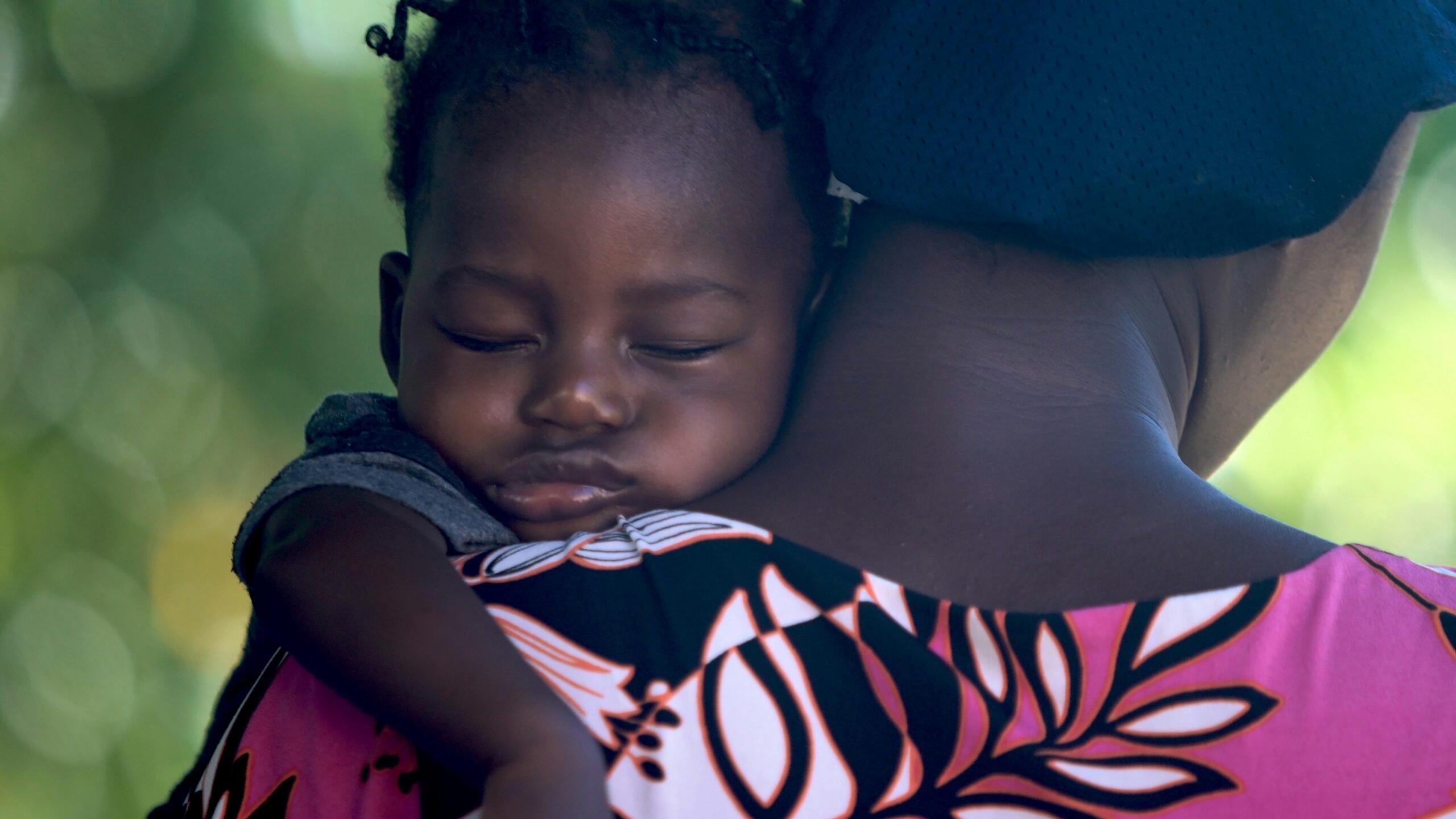 An image of a sleeping African newborn in the arms of a loved one.