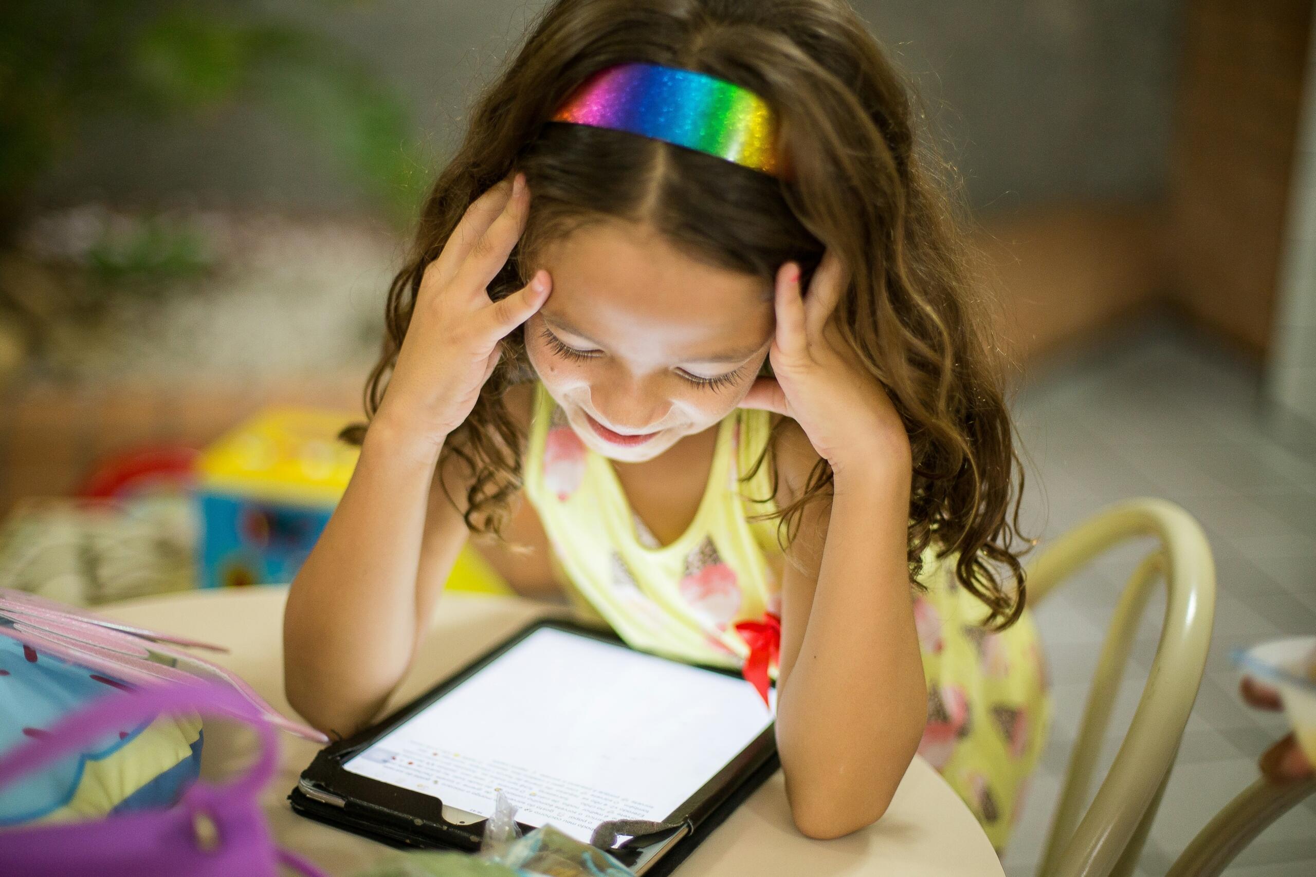 young child sitting at a table reading on e-reader