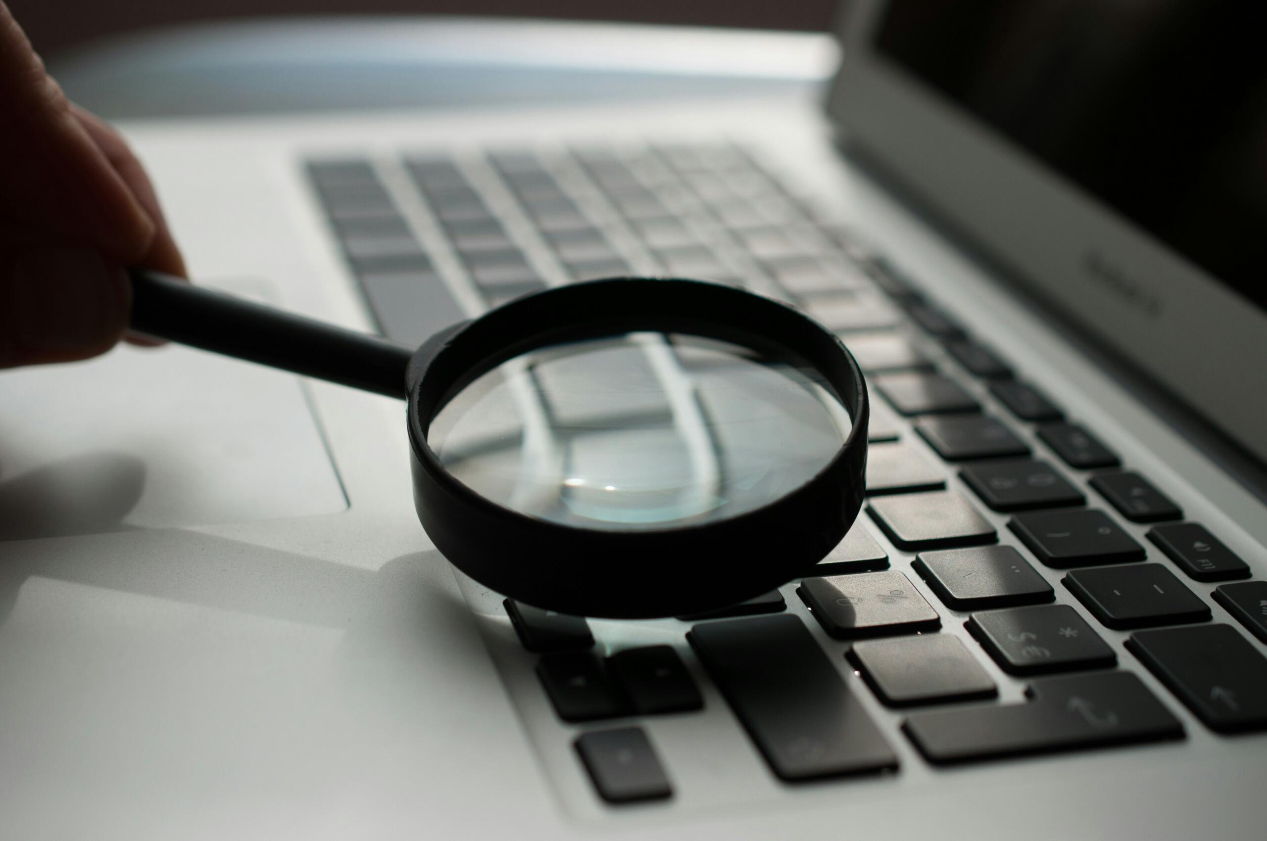 An image of a magnifying glass hovering over a laptop keyboard.