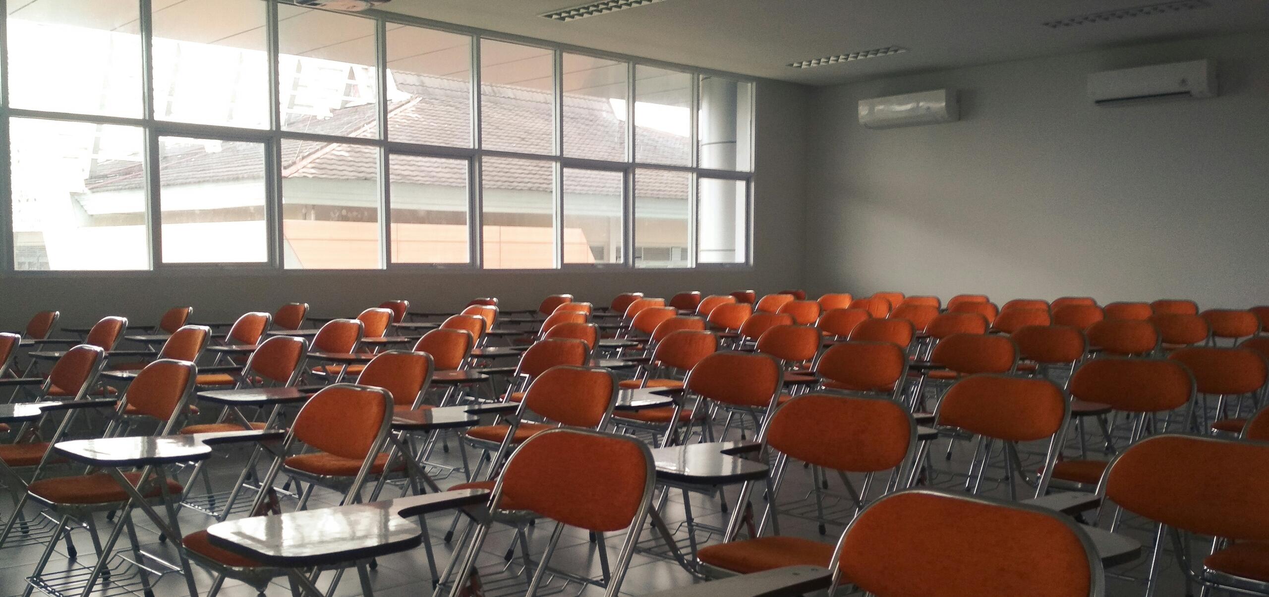 An image of an empty examination hall with rows of desks and chairs.