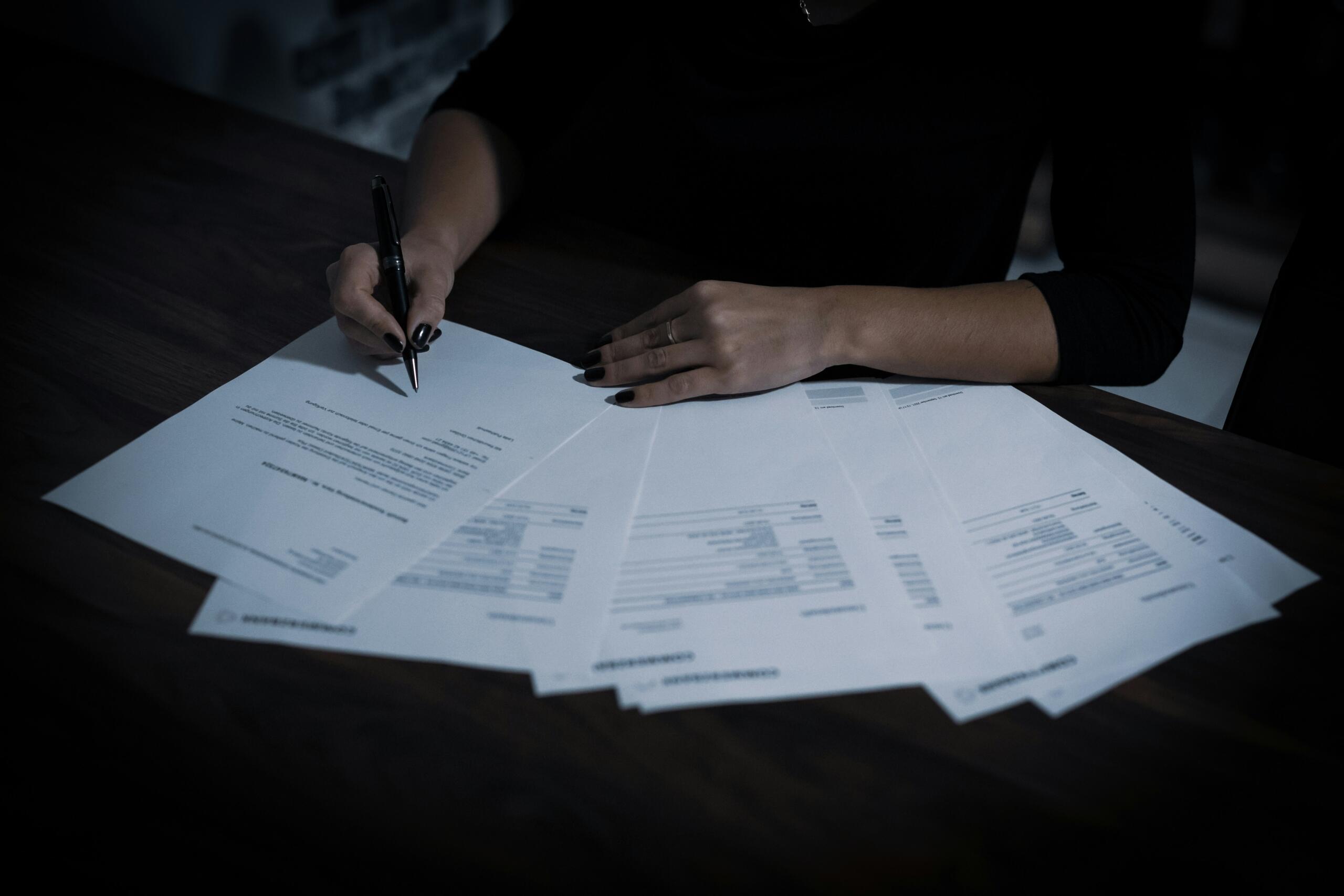 Person marking a examination papers with documents spread across a desk.