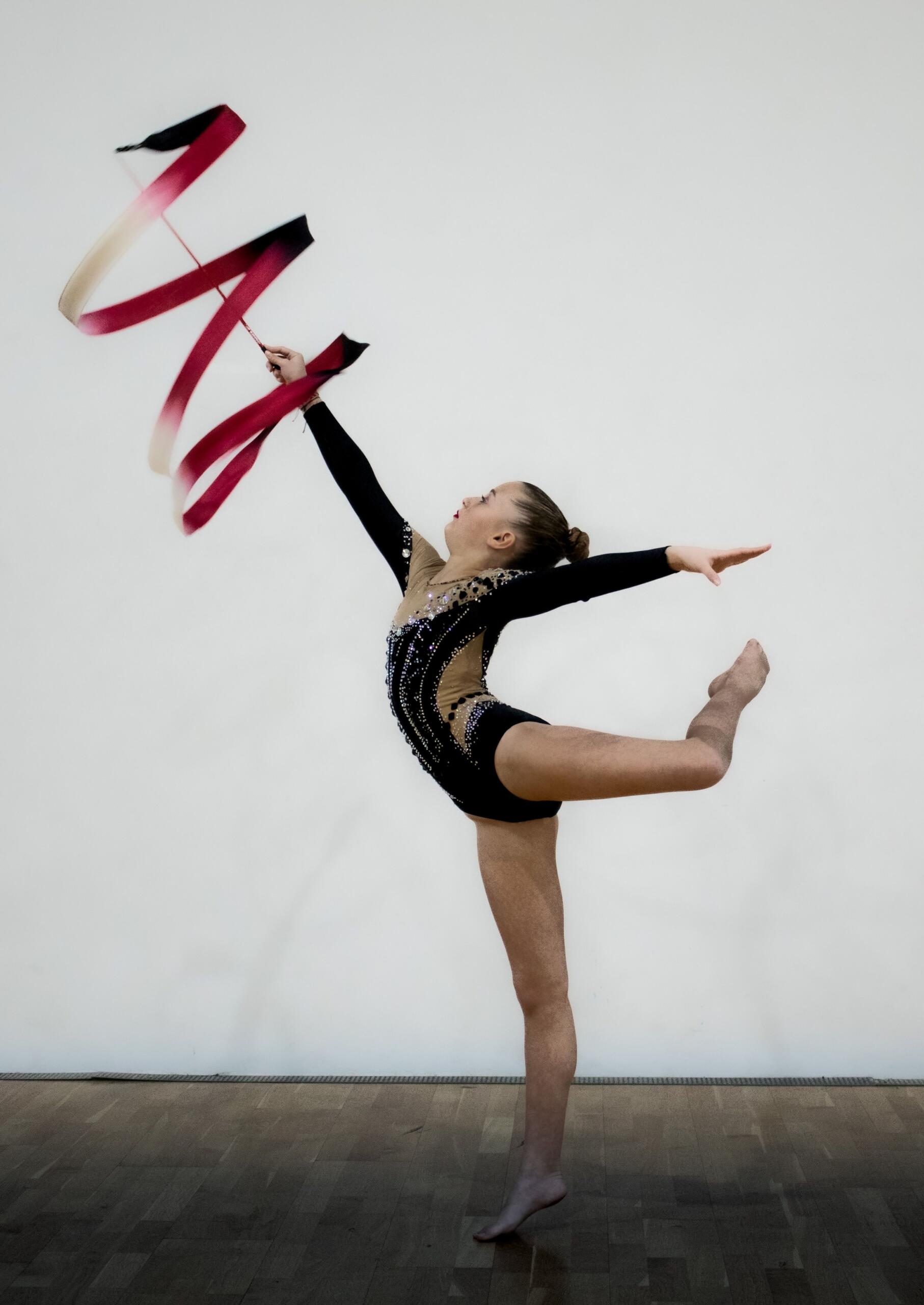 young girl in gymnast leotard twirling a ribbon on a stick