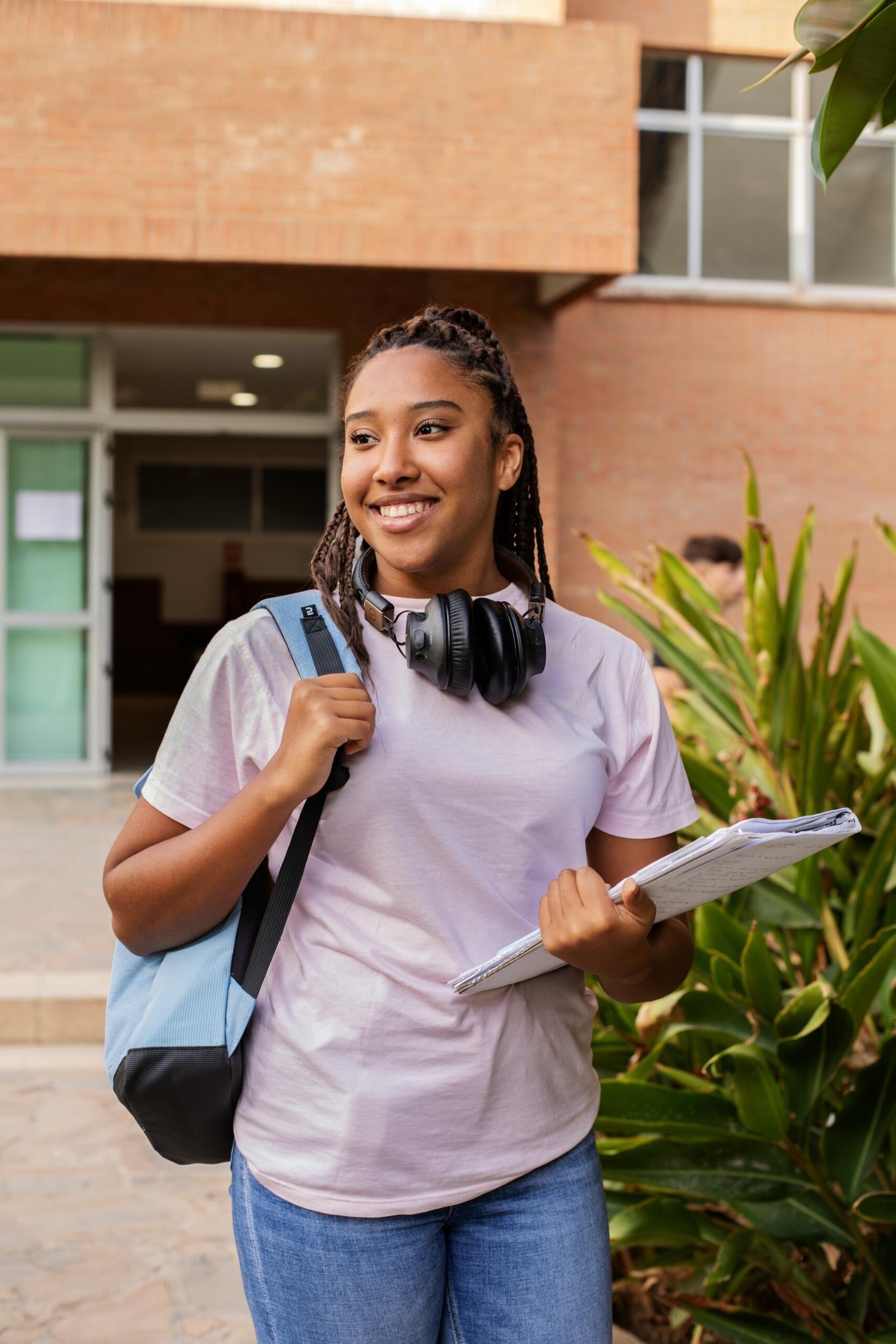 Student carrying books and a backpack outside a school building.
