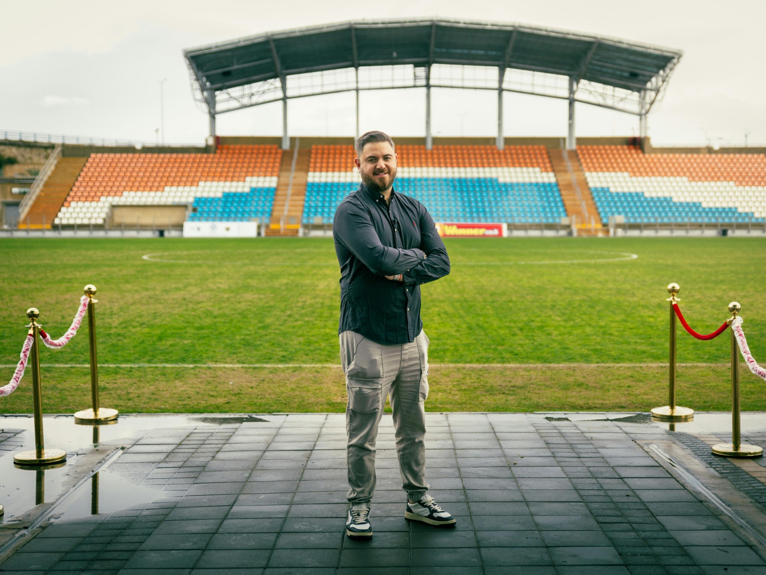 A man, possibly a scout, stands on the side of a soccer pitch.