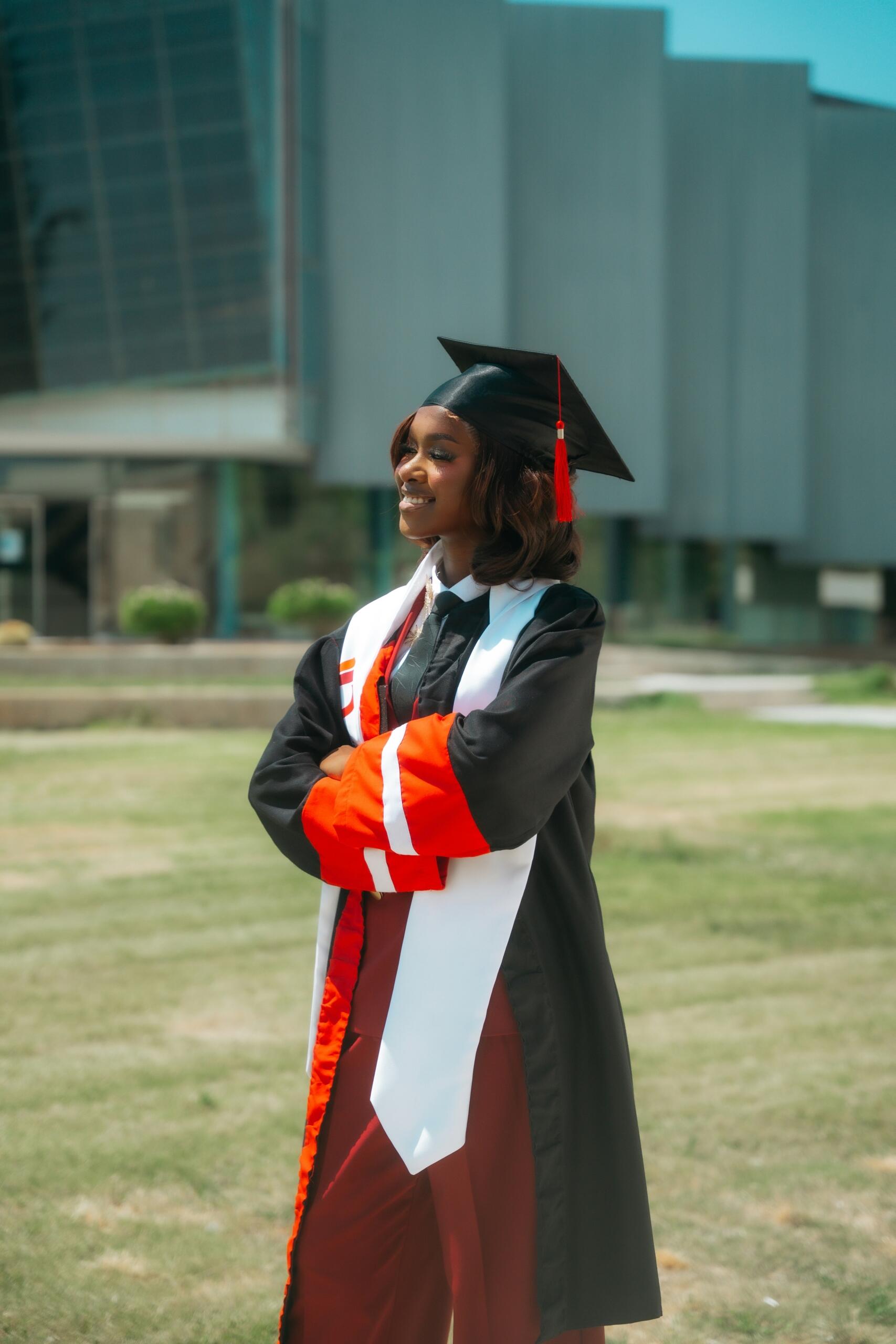 Graduate in cap and gown holding a rolled certificate outdoors on a university campus